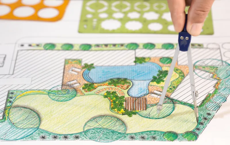 Landscape architect designing a backyard irrigation system with a compass, stencils, and a drawing of the backyard
